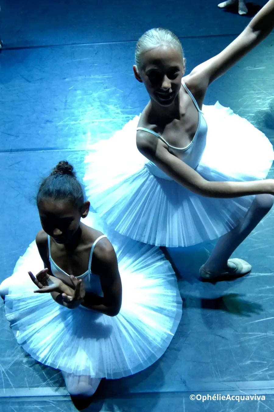 Deux jeunes élèves en tutu blanc assises sur la scène, en lumière bleue