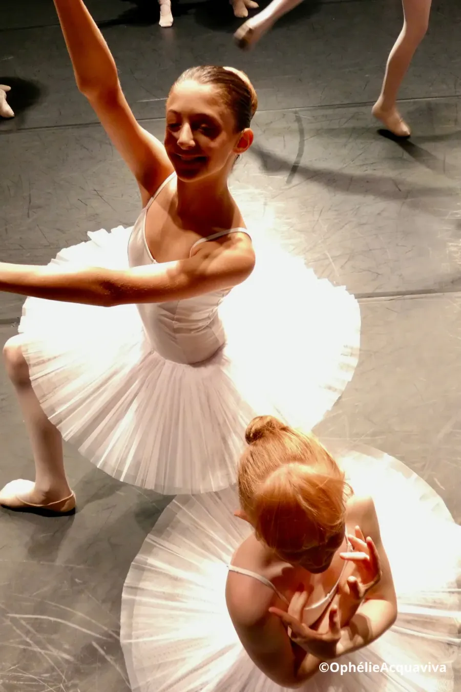 Deux élèves en tutu blanc, l’une bras tendu vers le public