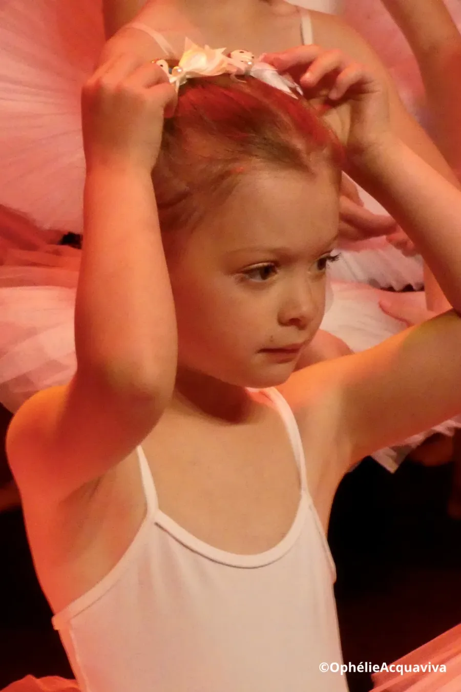 Une petite élève ajuste sa coiffure en coulisses, en tutu rose