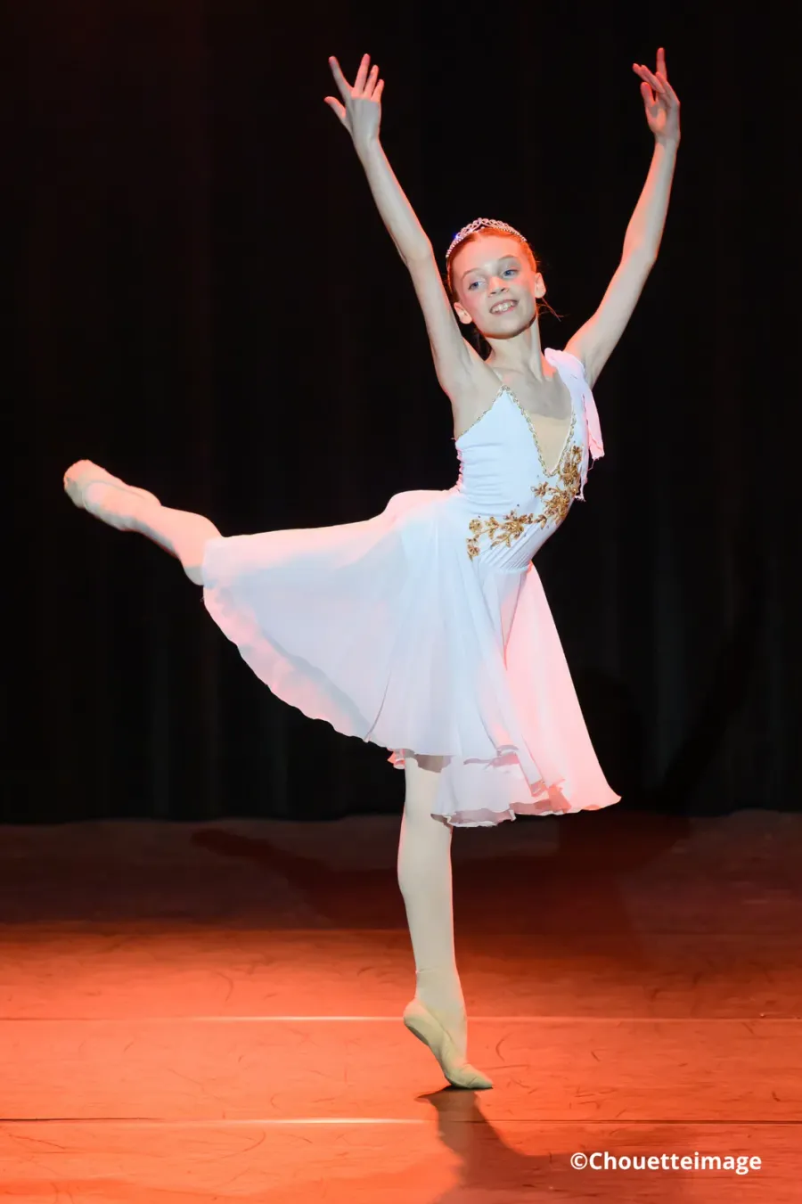 Une élève en robe blanche en pleine arabesque, seule sur scène